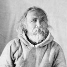 Photographic portrait of Mallikee wearing a skin parka and fur mittens; this photograph was taken in a studio and then placed in an oval frame. Fullerton, Nunavut, 1904-1905