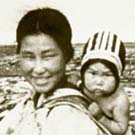 Photograph of an Inuit woman carrying an infant in a baby-pouch, unknown location, Nunavut, summer 1952