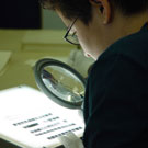 Photograph of Jesse Mike, an Iqaluit resident, using a magnifying glass to look at negatives at Library and Archives Canada, Ottawa, October 2005